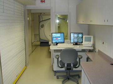 the inside of a mobile medical scanner room, with monitors, cupboards and an MRI scanner